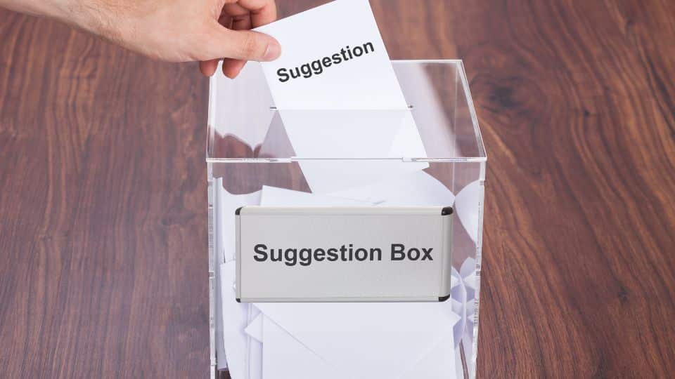 A hand of an employee putting a piece of paper to the suggestion box of the company